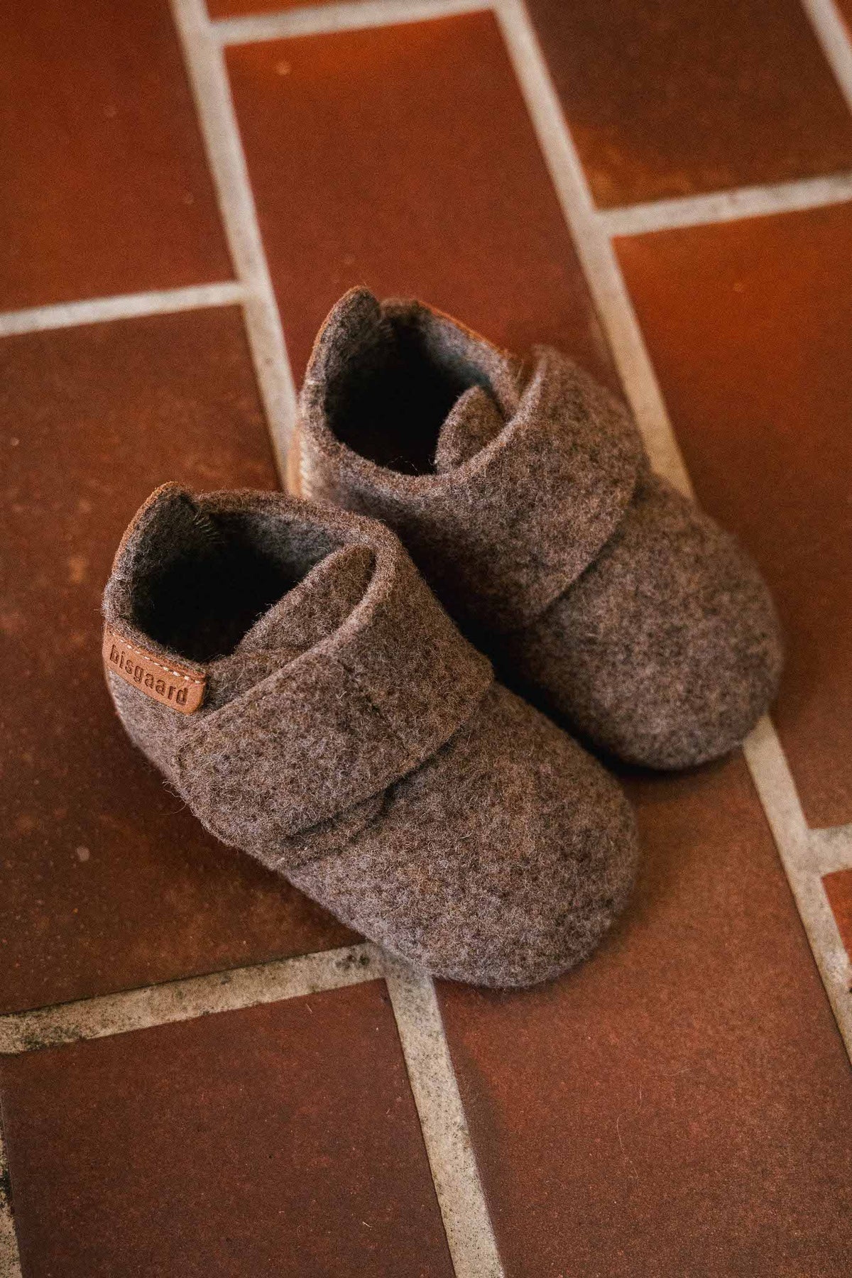 Baby Wool Camel – Babyhausschuhe aus Wolle – Bisgaard: zwei Schühchen auf einem Fliesenboden.