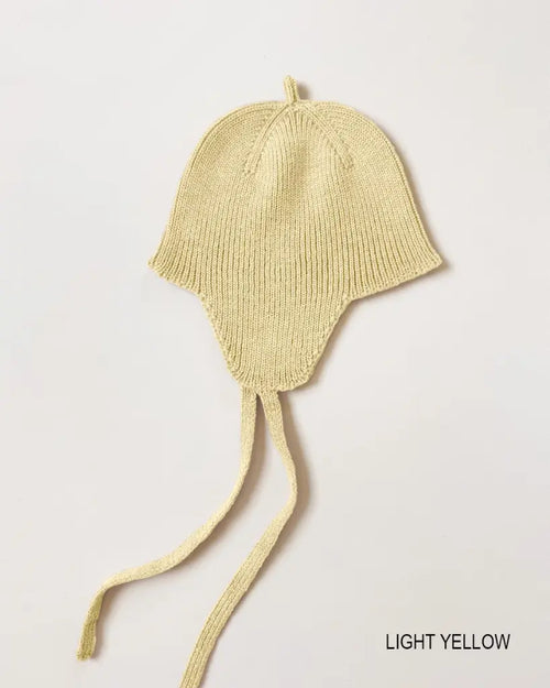 Bonnet Kota – Béguin pour bébé avec protège-oreilles – HVID : béguin pour bébé avec protège-oreilles et liens à nouer, photographié à plat.