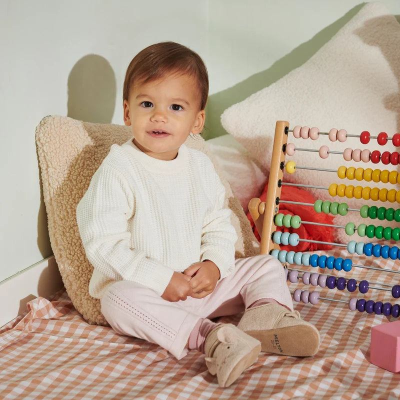 Mouse Wool Slippers – Wollen kinderslofjes met suède zool – MELTON: Baby sitzend zwischen Spielzeug mit den Hausschuhen an.