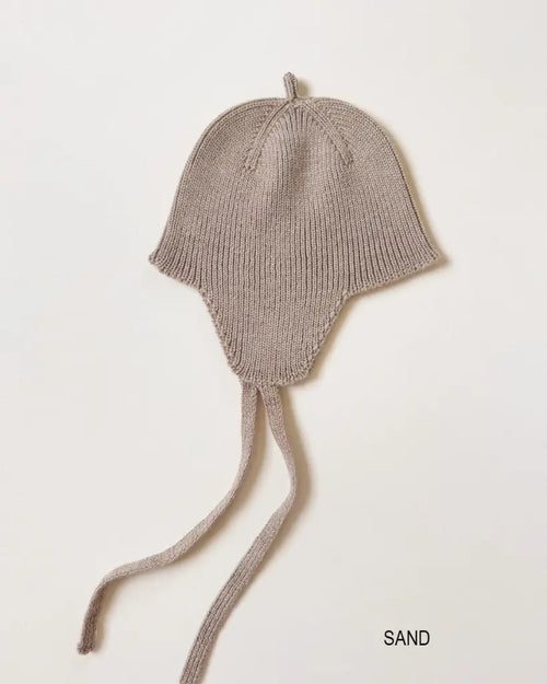 Bonnet Kota – Béguin pour bébé avec protège-oreilles – HVID : béguin pour bébé avec protège-oreilles et liens à nouer, photographié à plat.
