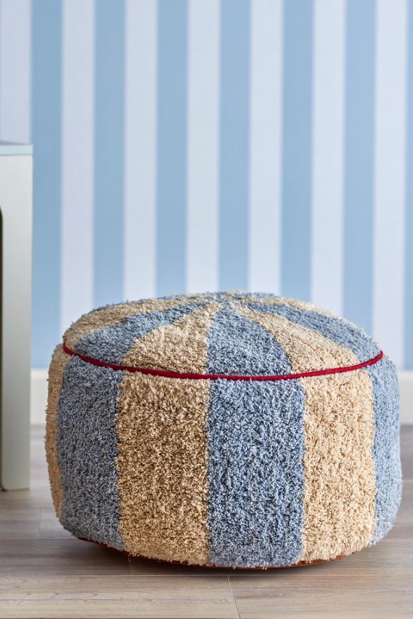 Charoline Pouf Multi – Bloomingville MINI : pouf devant un mur habillé de papier peint à rayures bleues.