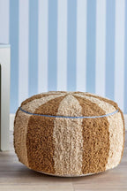 Charoline Pouf Brown – Bloomingville MINI: Pouf vor einer Wand mit blau gestreifter Tapete.