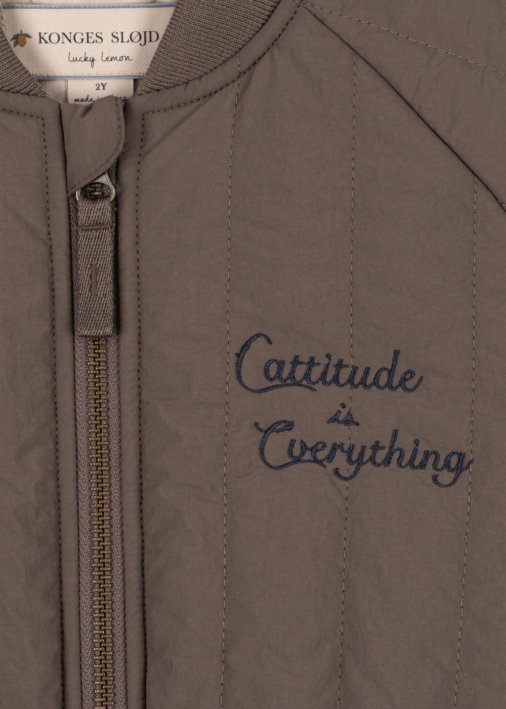 Thermo jacket Juno Bomber – Walnut – Konges Sløjd: detail of the zipper and embroidered text on the brown jacket.